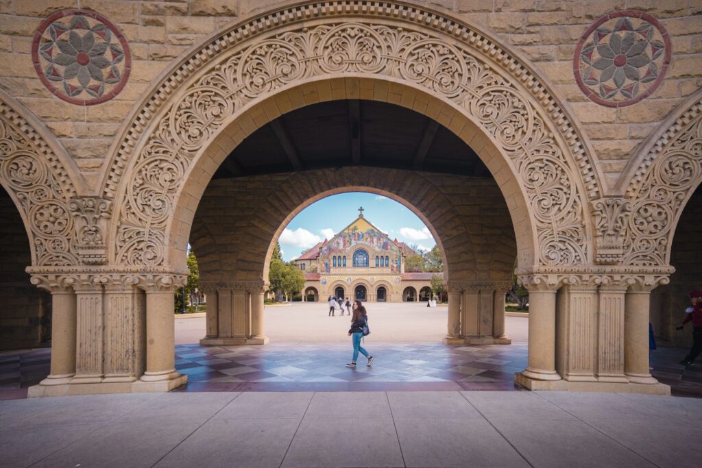 Person walking through a grand stone archway toward an ornate mosaic-tiled church on Stanford University campus