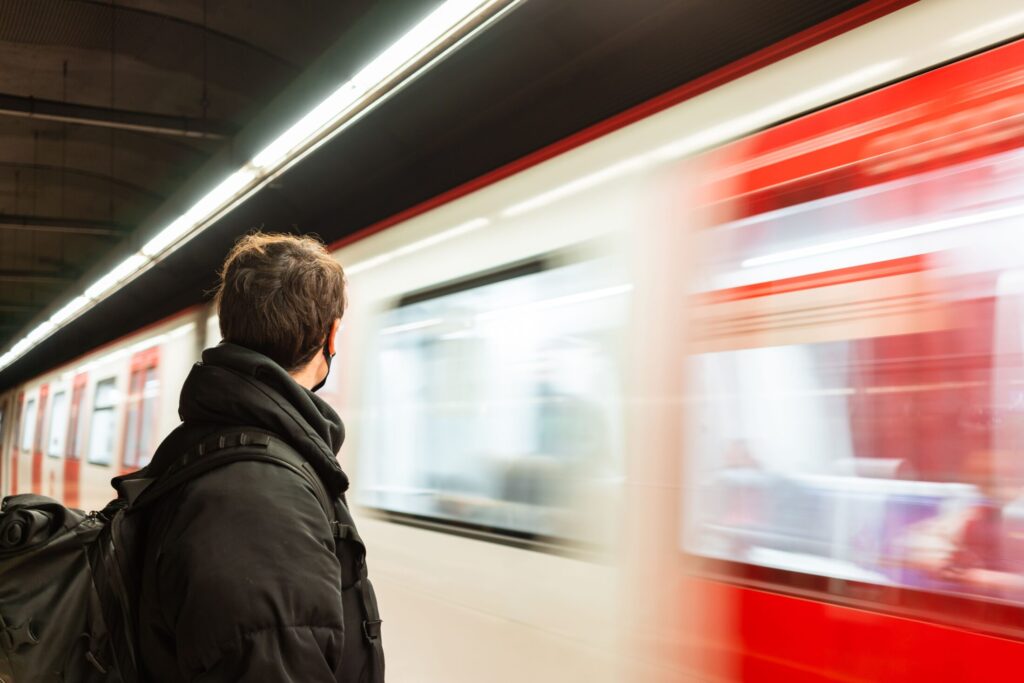 Commuter with a backpack waiting on a subway platform as a red and white train blurs past